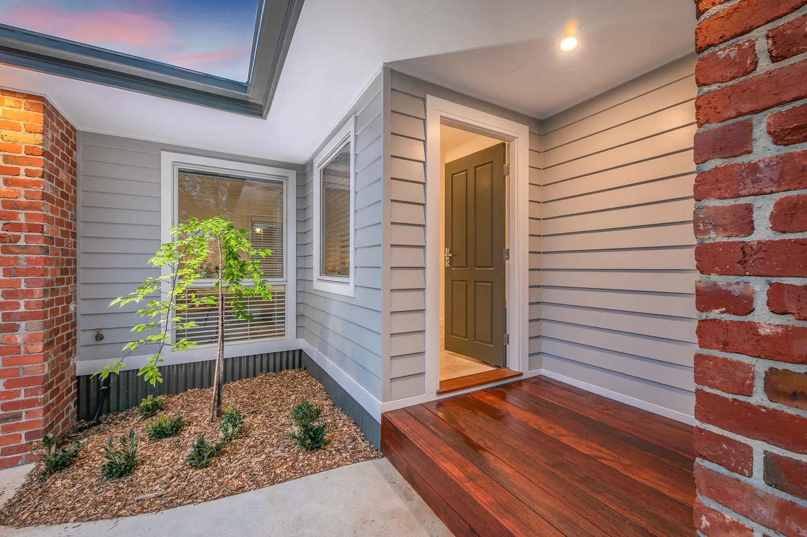 Entry porch with a dark front door, timber decked step and a freshly planted garden bed