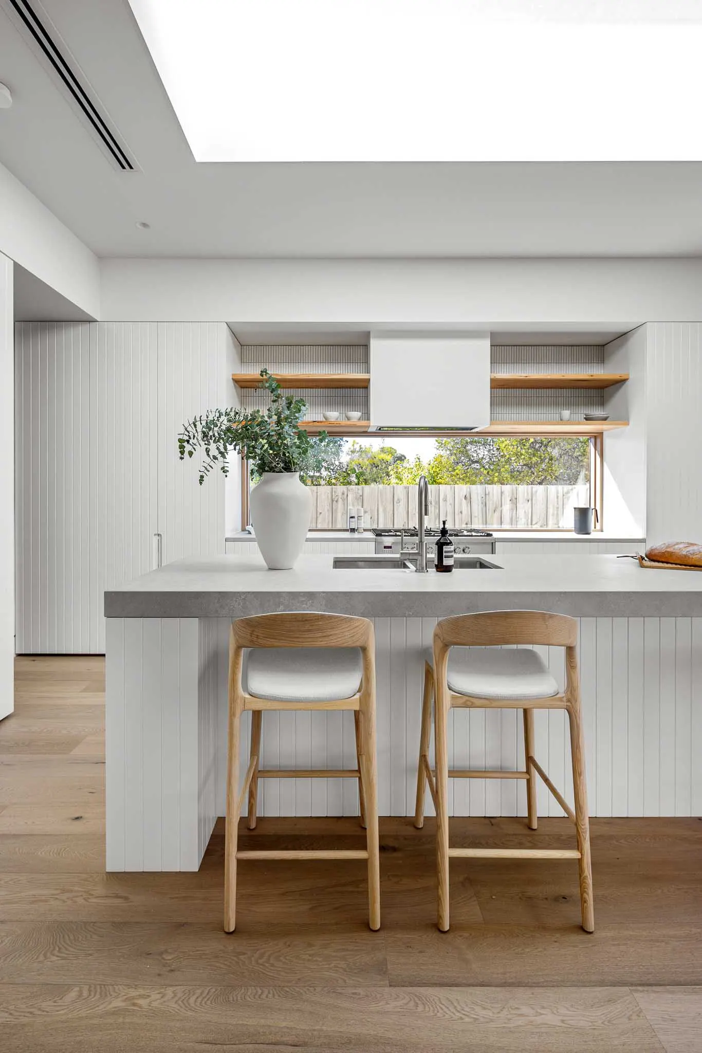 Peninsula bench and two oak stools facing a window splashback and timber open shelving