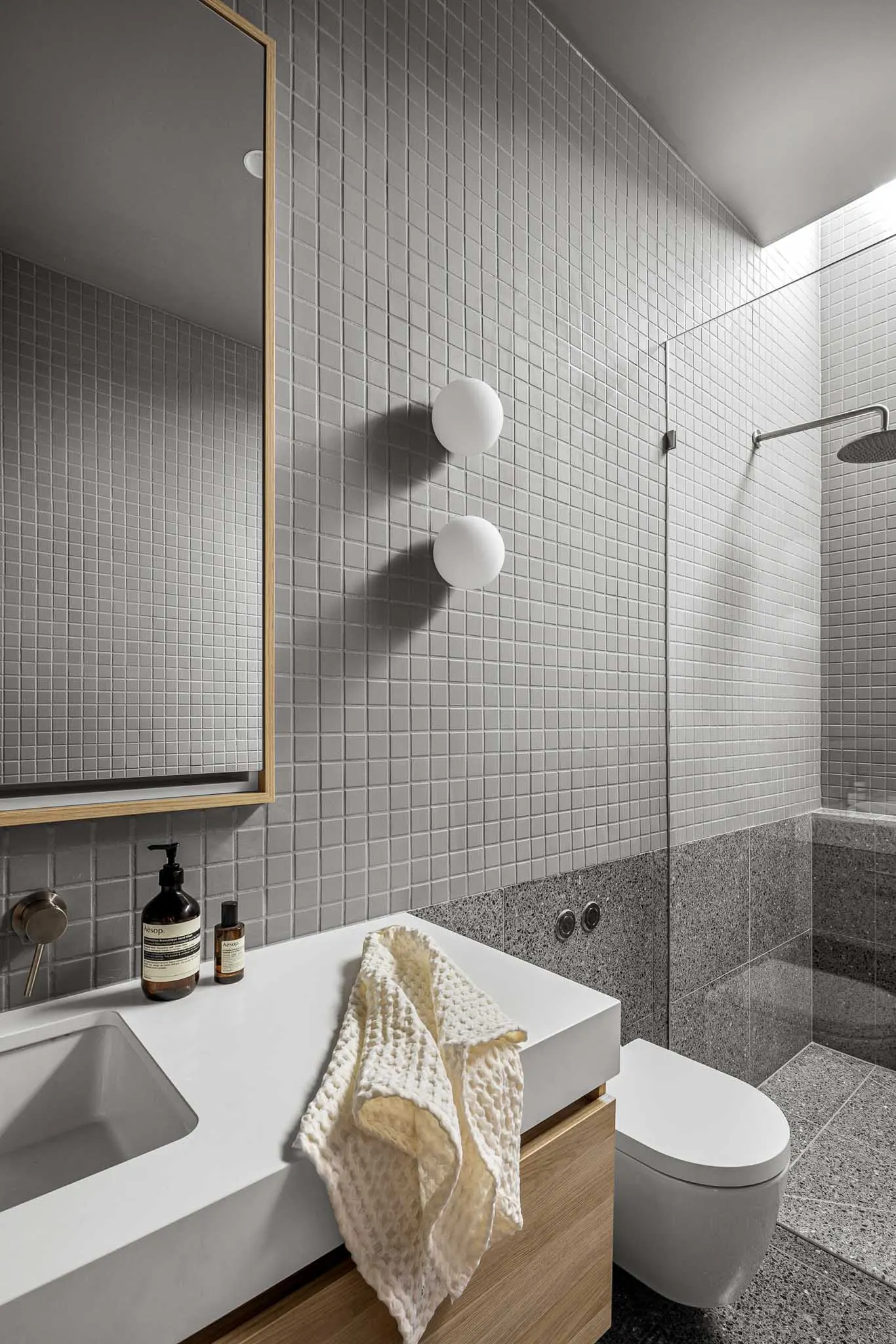 Ensuite in grey mosaic tile, timber-framed mirror and walk-in shower over terrazzo tiles