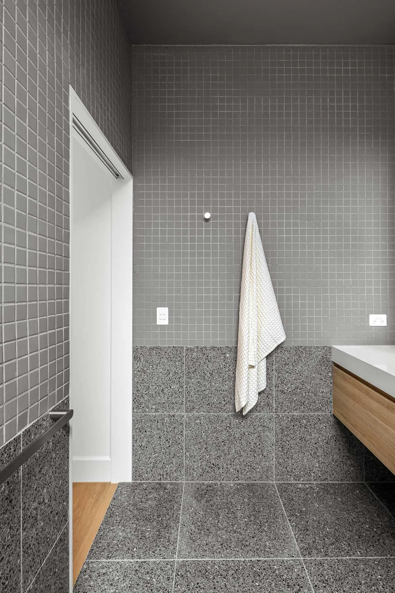 Grey tiled bathroom, terrazzo floor and lower walls, towel hung beside the doorway