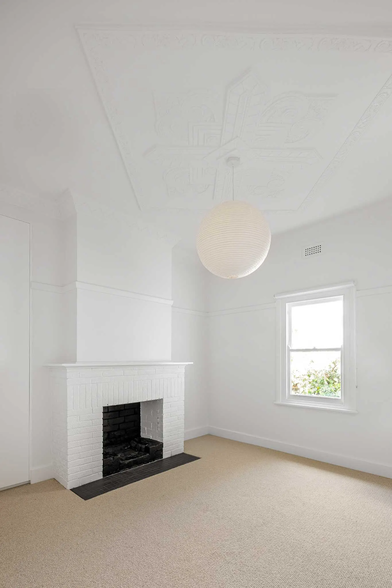 Bedroom with decorative pressed ceiling, white painted brick fireplace and paper globe pendant
