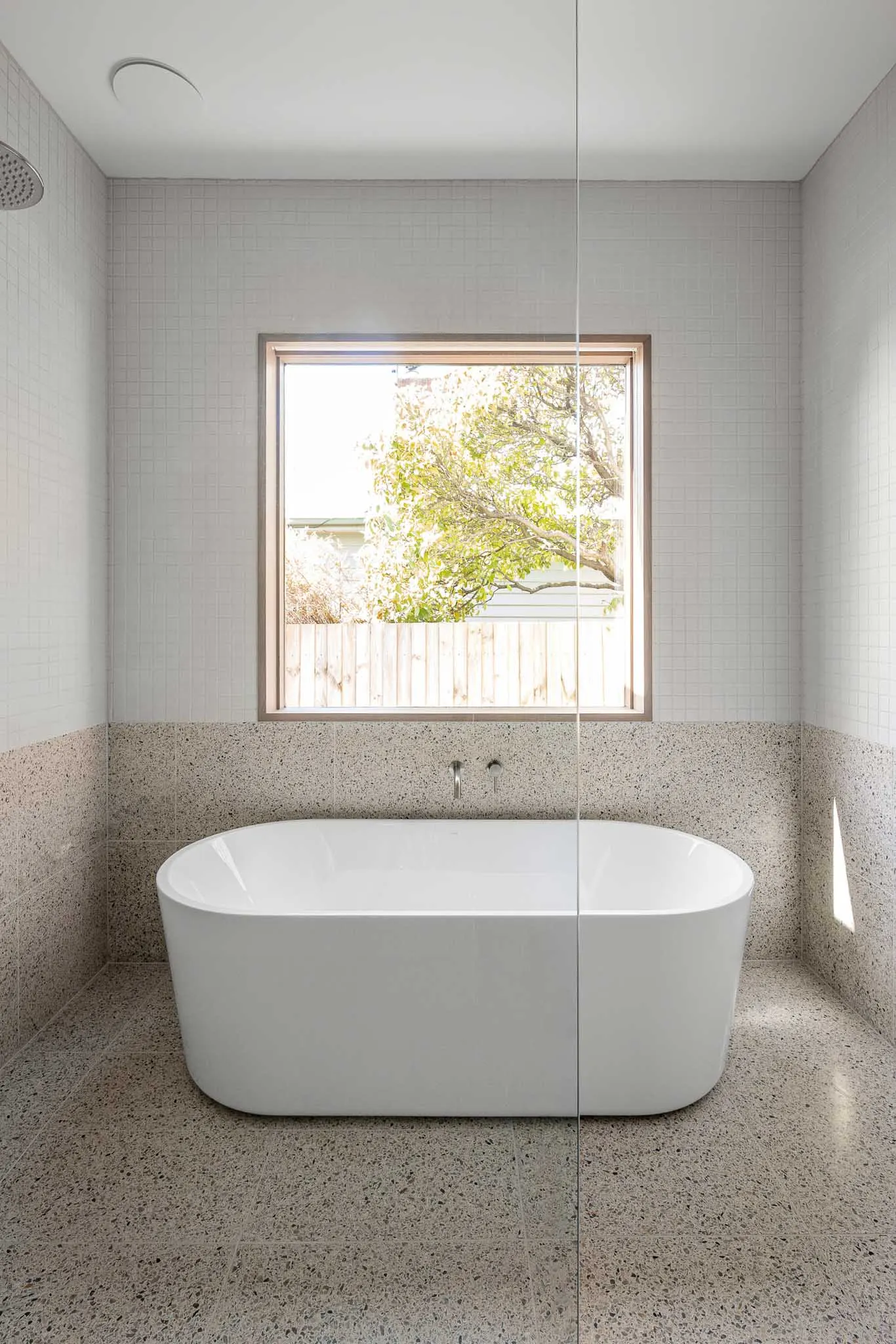 Freestanding bath below a timber-framed window, terrazzo tiling to floor and walls