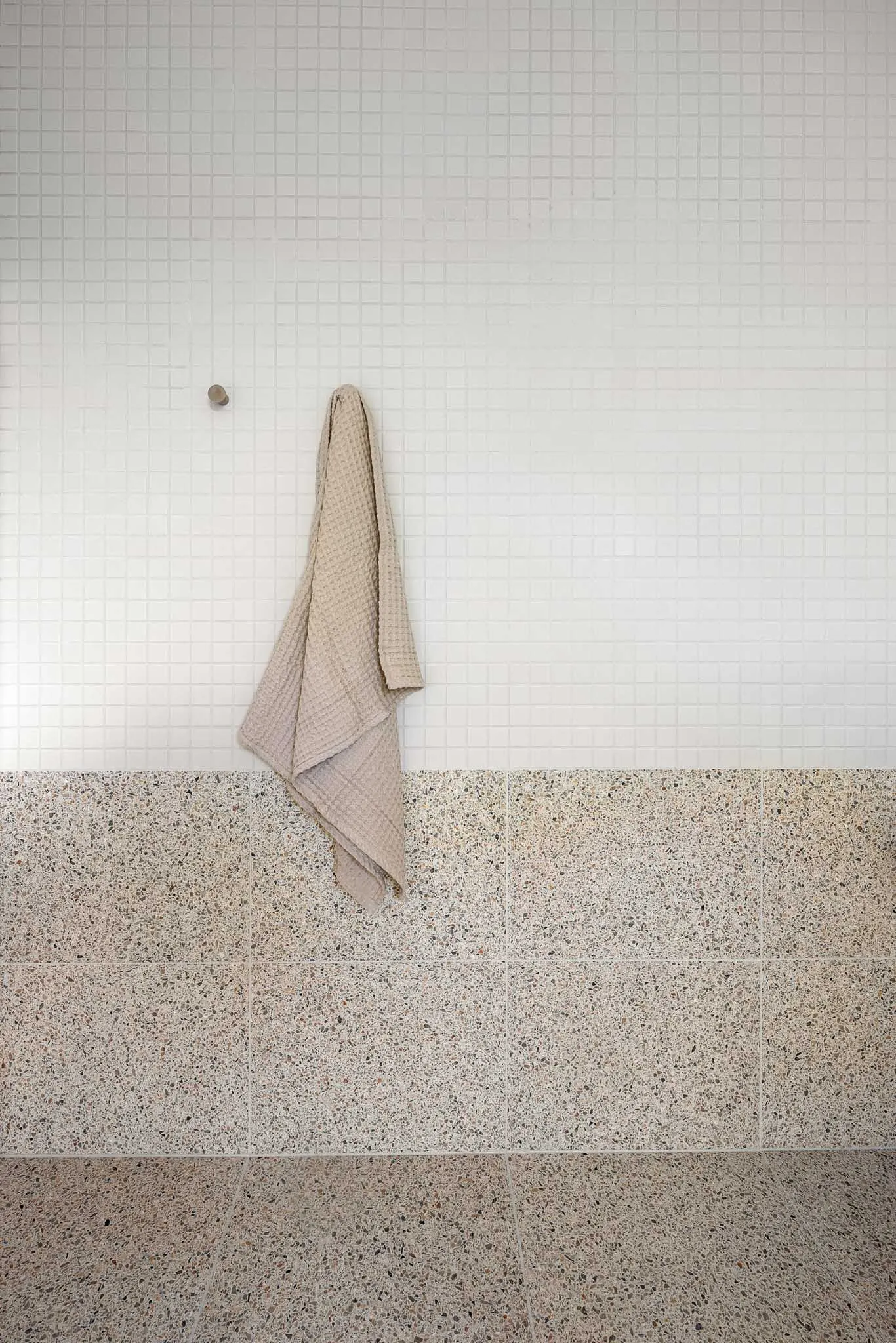 Waffle towel hanging on a white mosaic tiled wall above terrazzo floor tiles