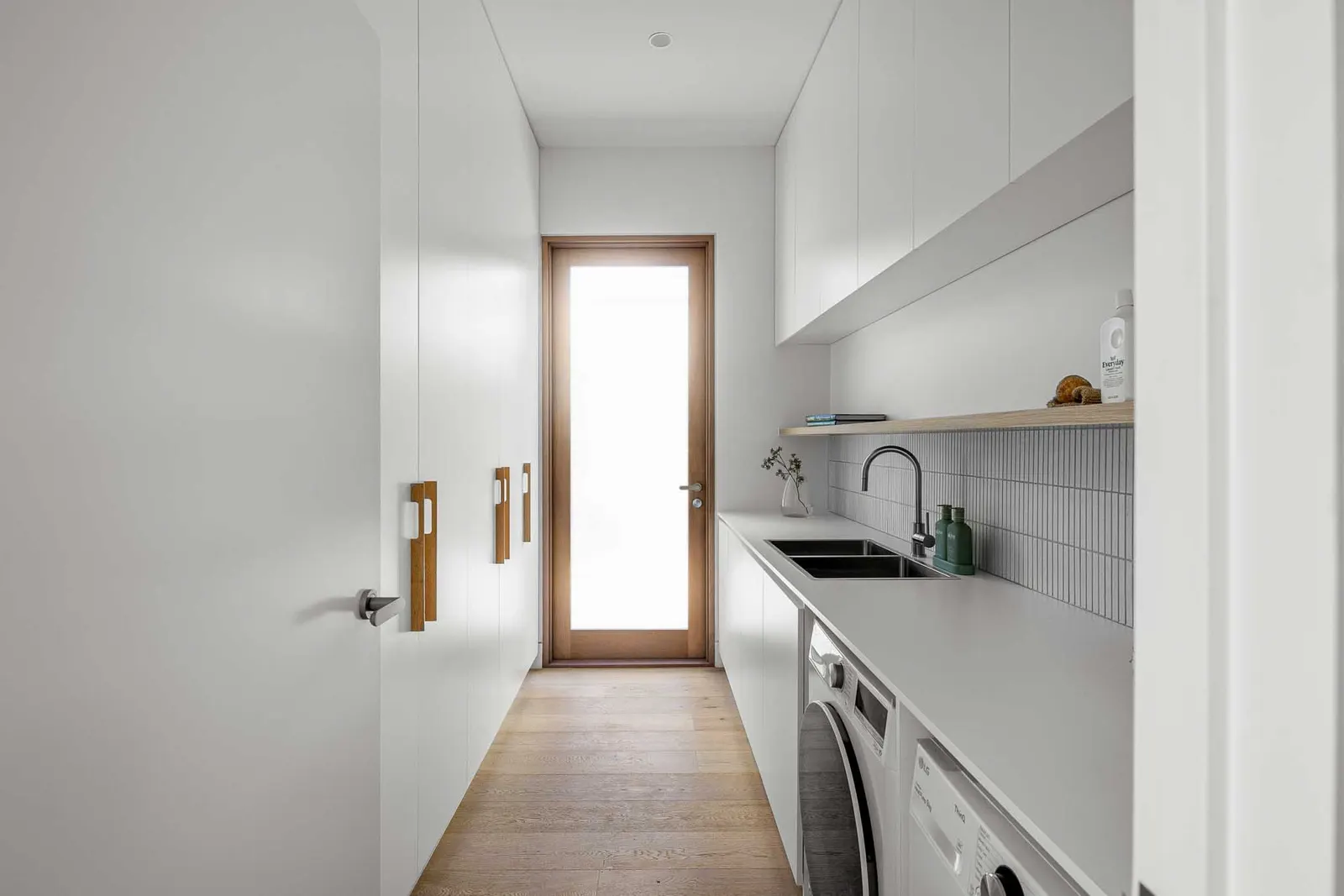 Galley laundry with stone benchtop, black tapware and a glazed timber door to outside