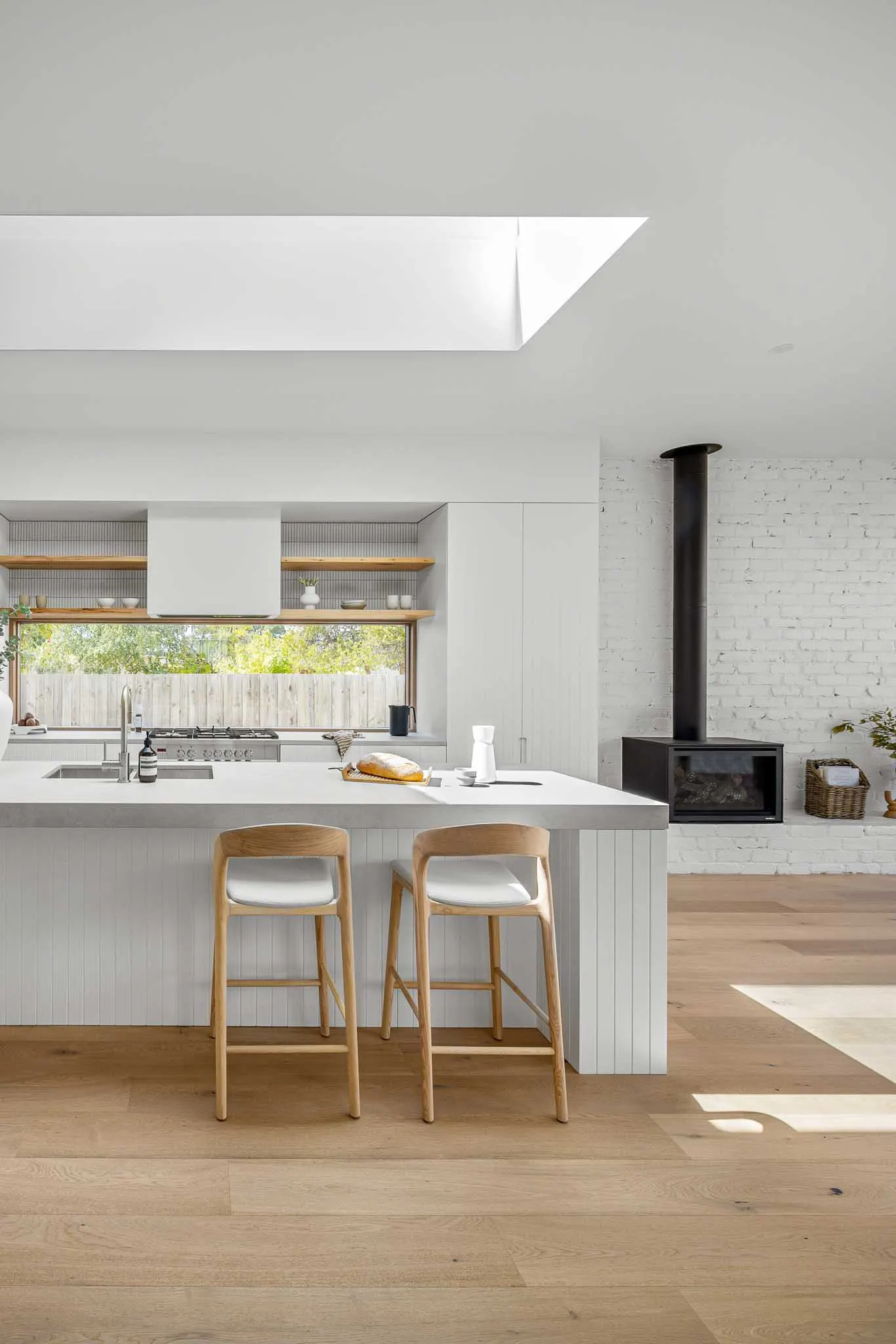 Skylight over the kitchen island, oak stools and the black wood heater set into white brick