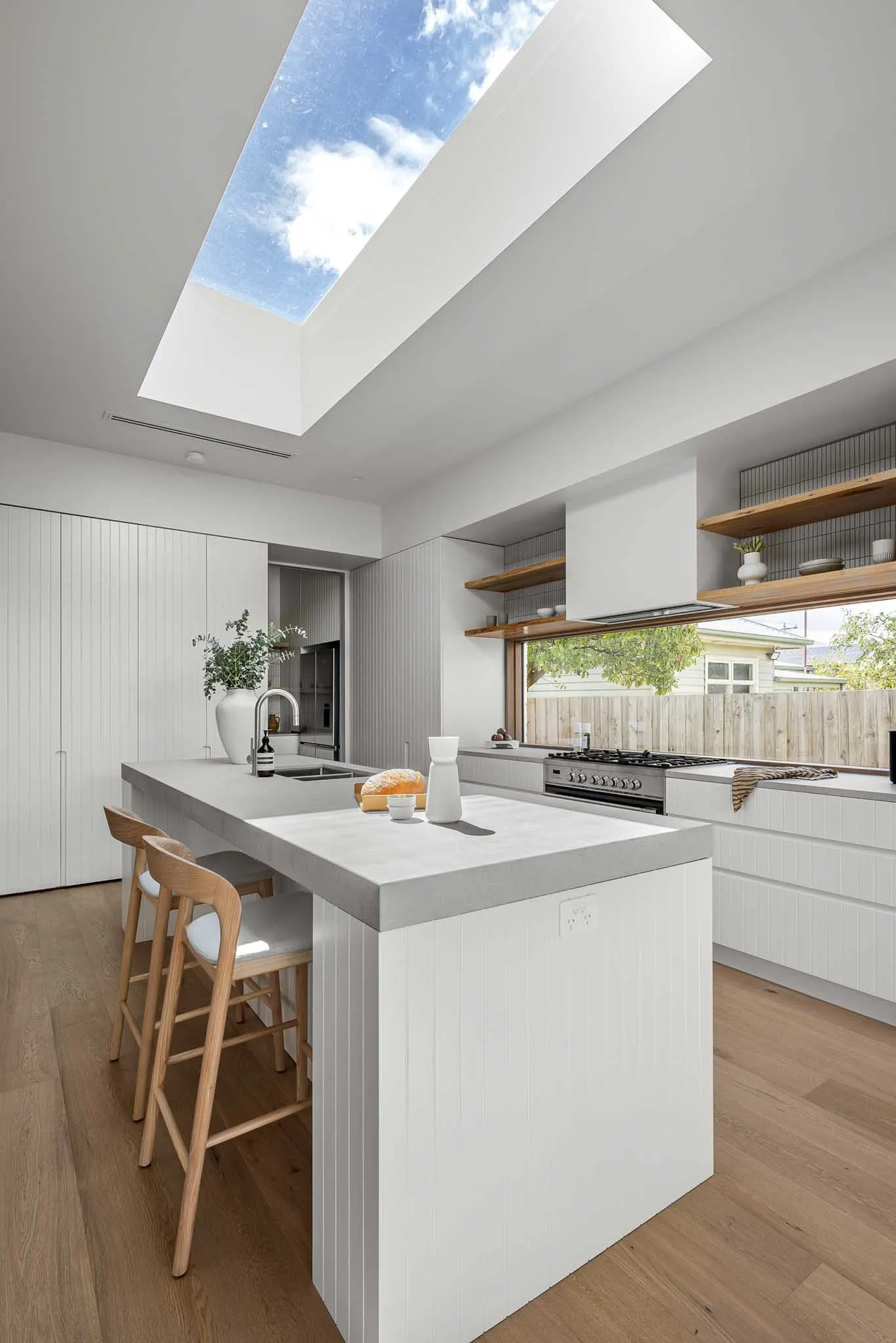 Sky through the kitchen skylight above a stone-topped island and fluted white joinery