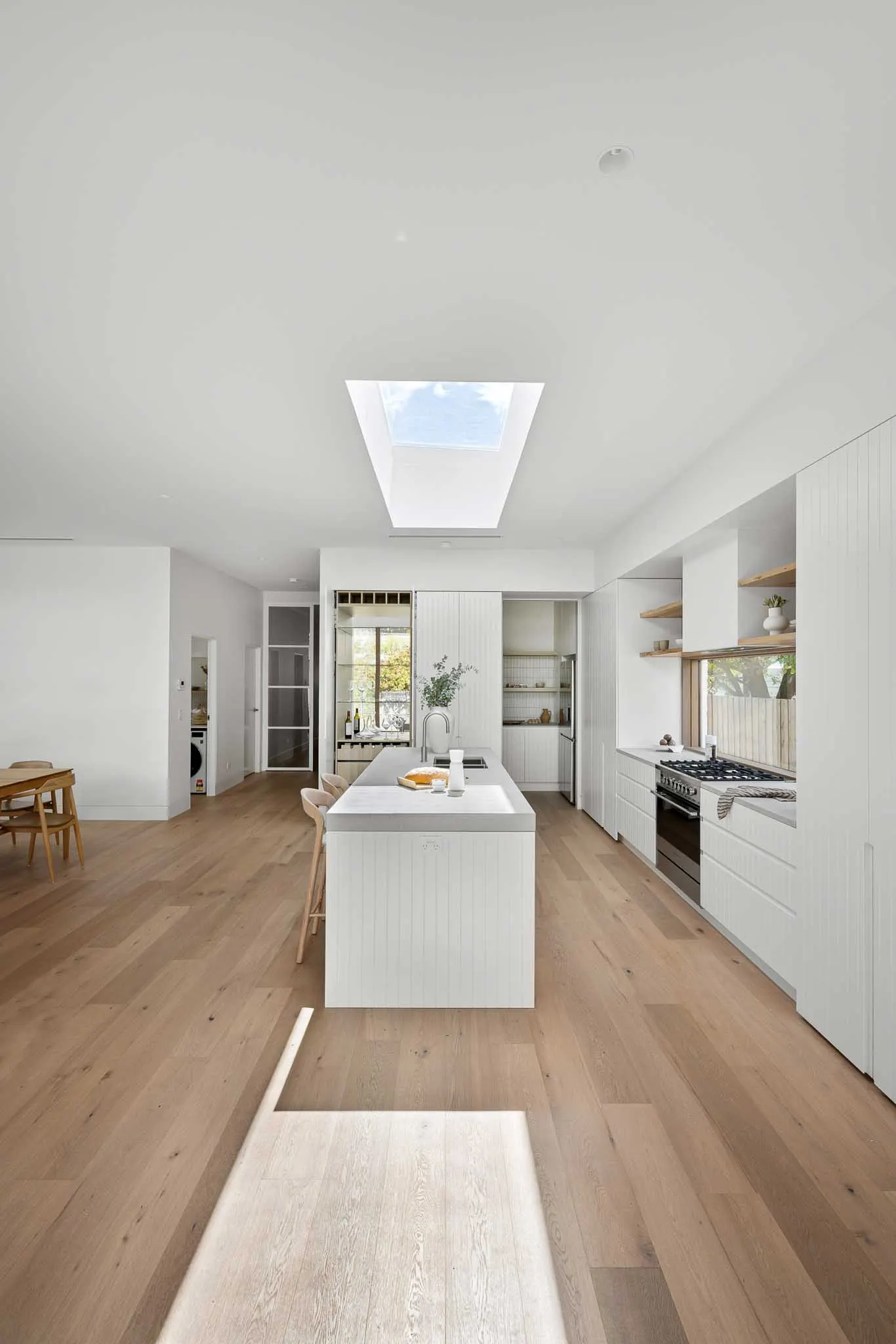 Long view down oak floorboards past the island to the dining zone, skylight overhead
