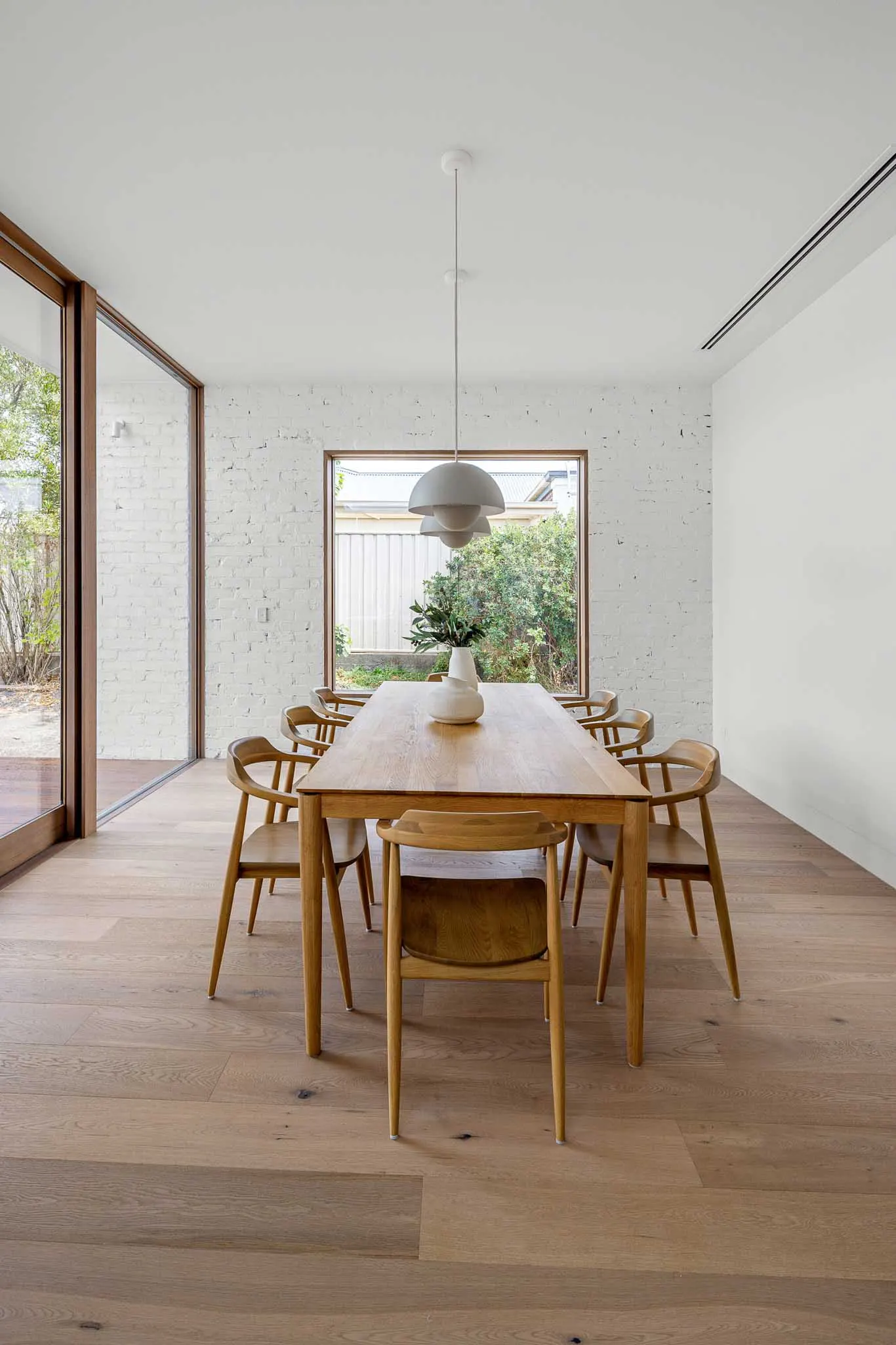 Oak dining table and spindle-back chairs beside a white brick wall and garden window, Yaldwyn St