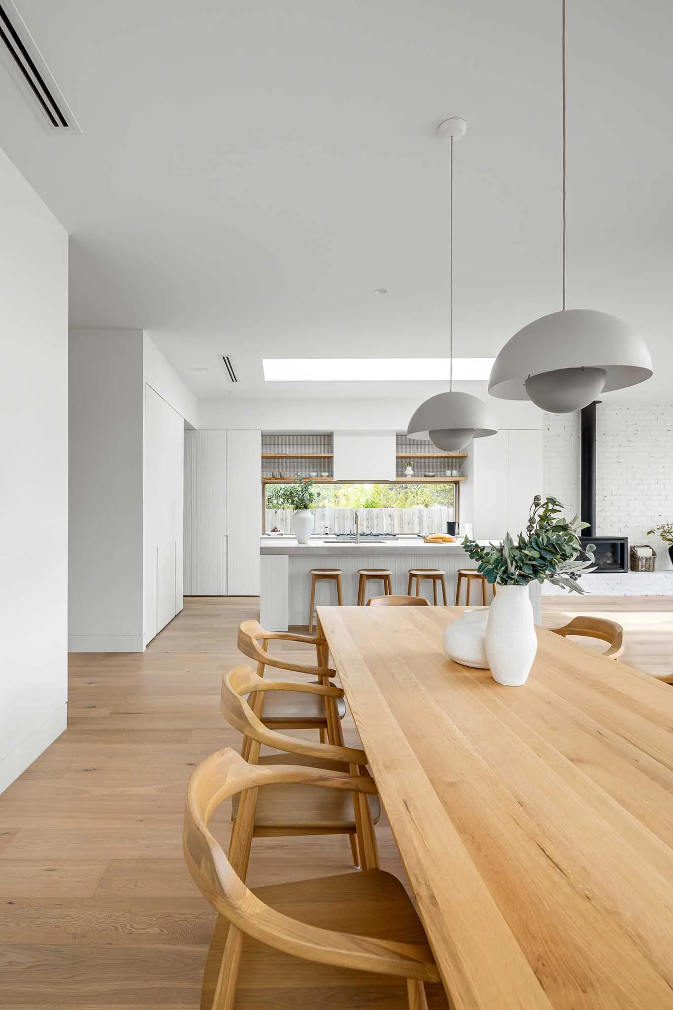 Dining table with carver chairs and dome pendants, kitchen and wood heater beyond