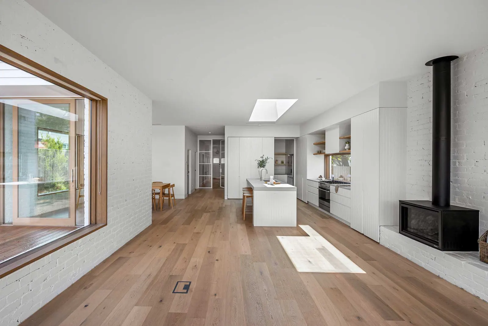 Open-plan living, dining and kitchen at Yaldwyn St, Kyneton, oak floors and white brick walls